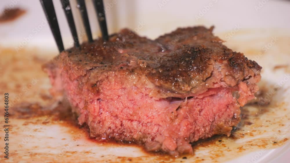 A large piece of freshly grilled beef steak on a plate. Medium-roasted meat with blood in slow motion. A knife and fork cut a piece close up view. A large piece of freshly grilled beef steak on a plate. Medium-roasted meat with blood in slow motion. A knife and fork cut a piece close up view.