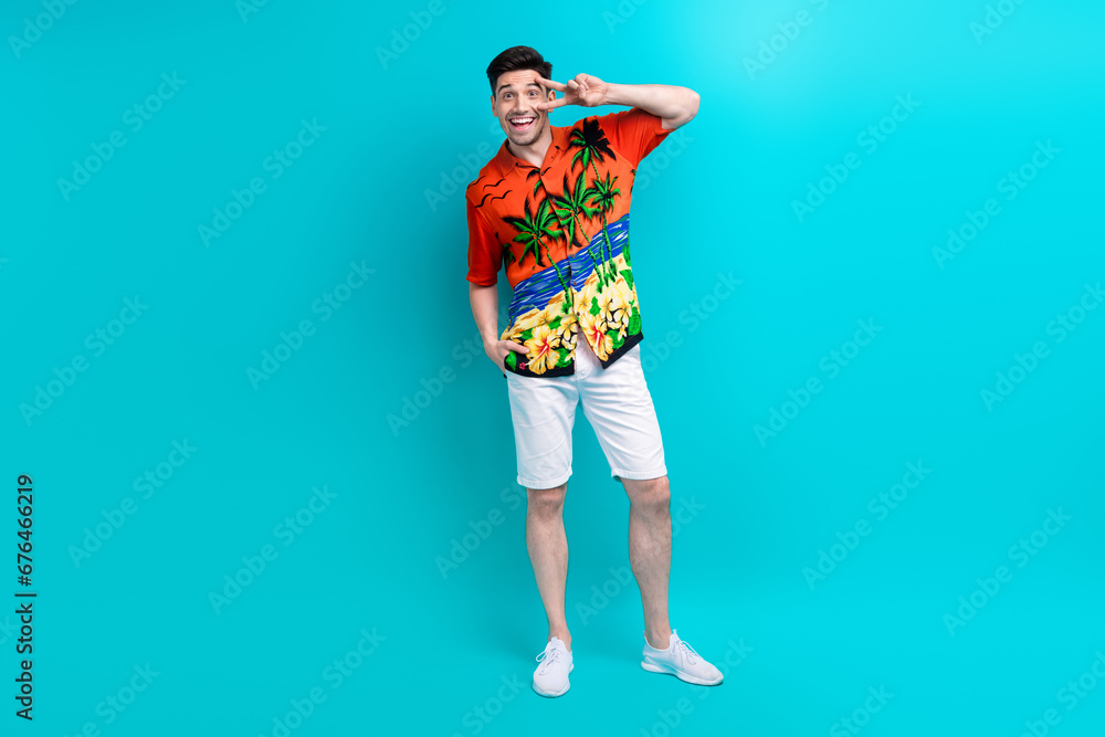 Fototapeta premium Full size photo of cheerful funky impressed guy wear tropical shirt stylish shorts show v-sign on eye isolated on blue color background