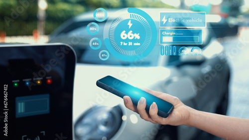 Modern businessman check battery status from smartphone mobile 3D hologram while his EV car recharging energy from charging. Innovative technological advancement of future EV automotive tech. Peruse