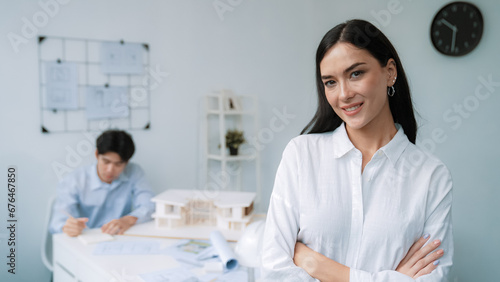 Closeup of female professional architect engineer cross arms with confident while skilled coworker focus on drawing blueprint at table with house model. Creative living and design concept. Immaculate.