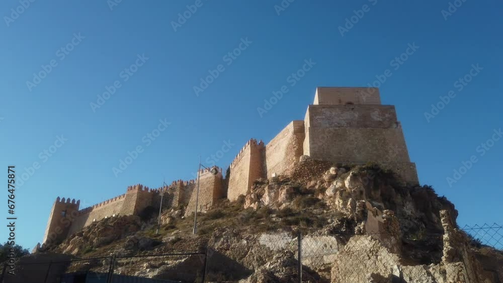 Alcazaba castle on a cliff behind a chain fence under a clear blue sky Alcazaba castle on a cliff behind a chain fence under a clear blue sky