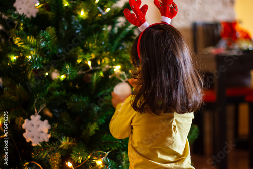 Girl putting a ball on Christmas tree with reindeer antler headband