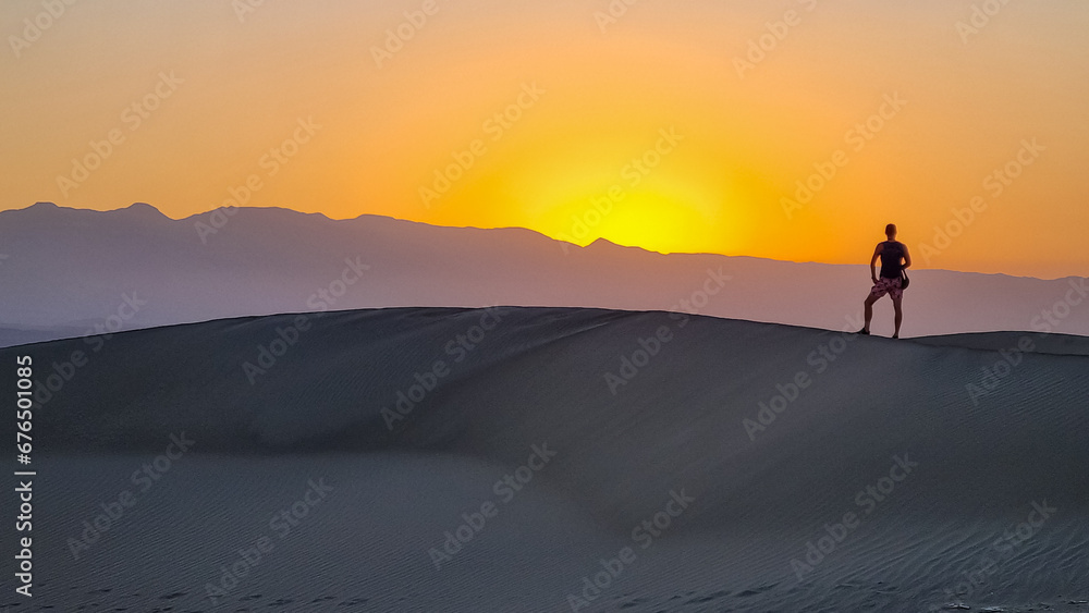 Silhouette of man enjoying the sunrise with scenic view on Mesquite Flat Sand Dunes, Death Valley National Park, California, USA. Morning walk in Mojave desert with Amargosa Mountain Range in back
