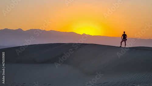 Silhouette of man enjoying the sunrise with scenic view on Mesquite Flat Sand Dunes, Death Valley National Park, California, USA. Morning walk in Mojave desert with Amargosa Mountain Range in back photo