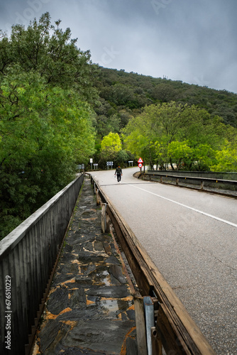 Latino guy strolling on bridge, rainy fall day, scenic countryside.