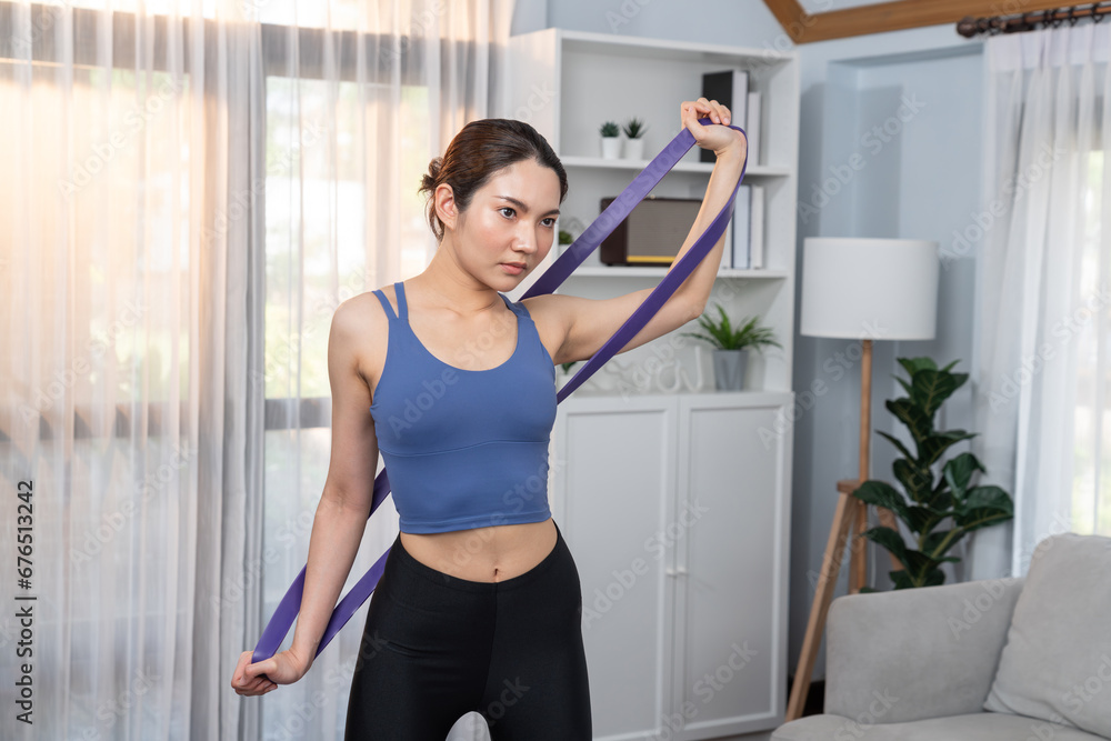 Vigorous energetic woman doing exercise at home, stretching resistance sport band for muscle gain. Young athletic asian woman strength and endurance training session as home workout routine concept.