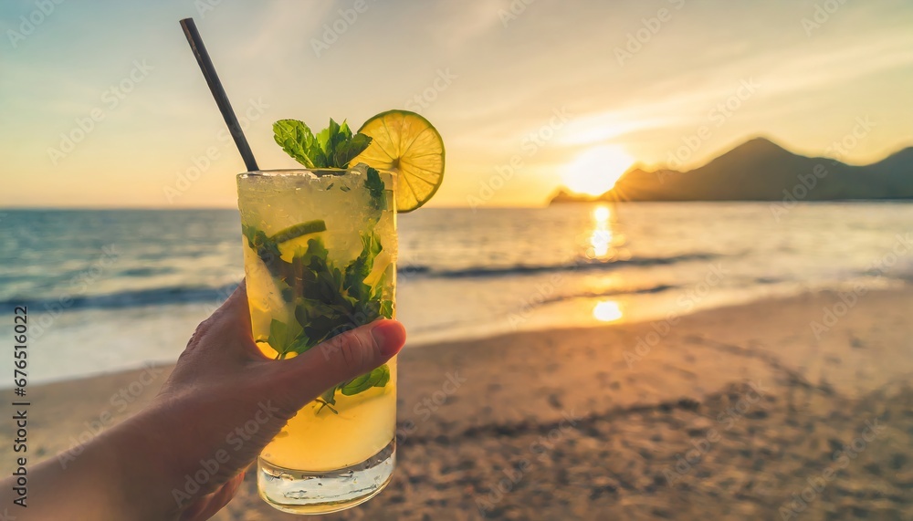 Hand holding mojito cocktail on beach, fresh summer drink with lime and mint, tropical paradise resort background with sea view - obrazy, fototapety, plakaty 
