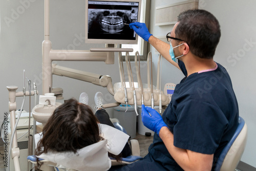 dentist gives information to her patient by showing dental x-ray showing.  Medical teeth care taker pointing at patient radiography on screen.  Tooth removal concept. Dental implants concept. photo