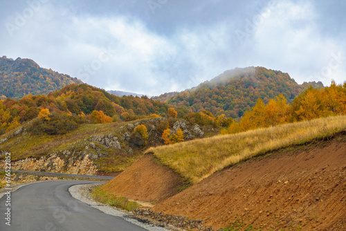 Winding road to the mountains. Sunny autumn in the mountains covered with bright colorful trees.