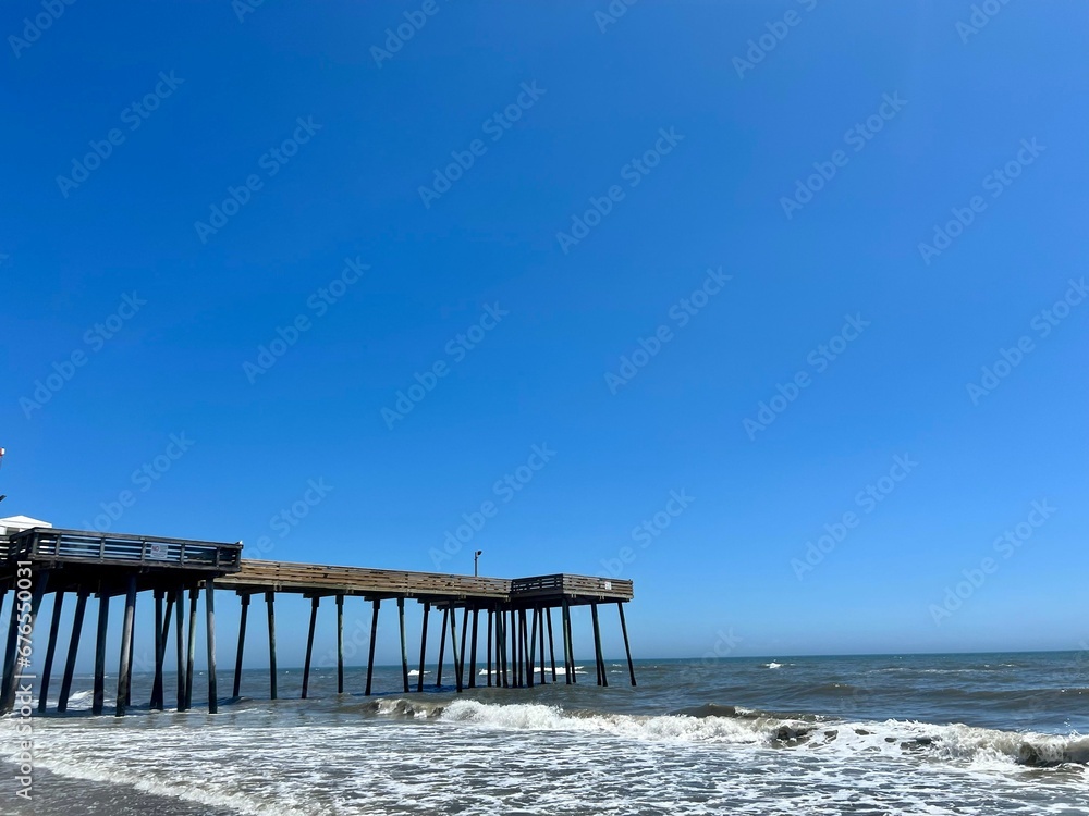 Scenic shot of a wooden fishing pier on the beach against the blue sky Scenic shot of a wooden fishing pier on the beach against the blue sky