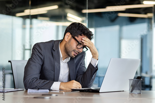 Depression at workplace, businessman disappointed with achievement results sad in despair inside office, man in business suit unhappy working with laptop.