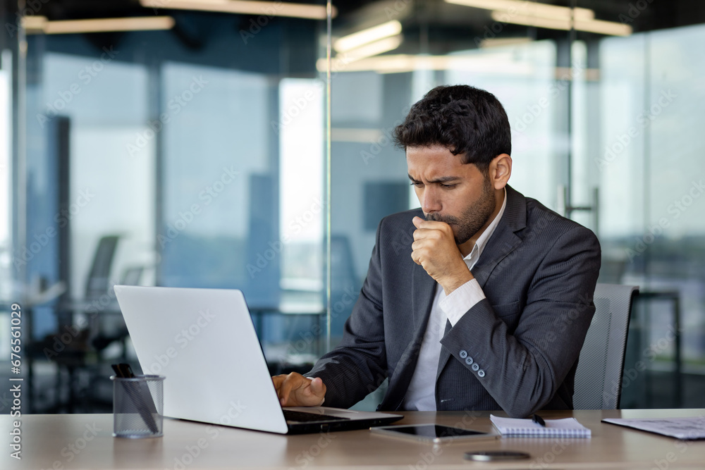 Sick businessman coughing inside office at workplace, man in business suit working with laptop, cold with flu. Sick businessman coughing inside office at workplace, man in business suit working with laptop, cold with flu.