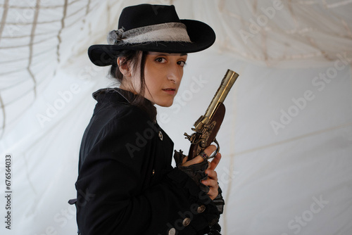 A pirate lady in a hat with a vintage pistol in her hands  a beautiful young brunette in a pirate costume  sails on the background