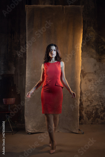 A femme fatale in a red dress. Attractive brunette in an elegant dress. photo in dark colors on a textured wall, warm light