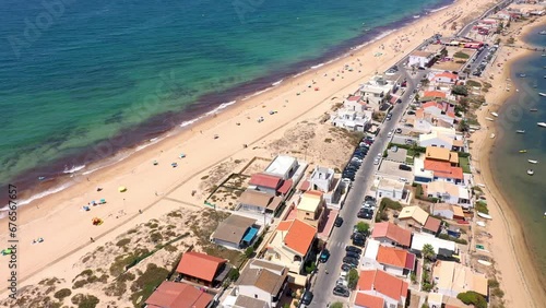 Aerial view of ocean coast and beach. Boats on the water and tourists relaxing on beach as seen from a drone. Praia de Faro Algarve Portugal. road in the middle of the island