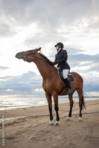 Equestrian sports. Horsewoman and her horse on the beach, portrait on the background of the sea, horseback riding outdoors © Ulia Koltyrina
