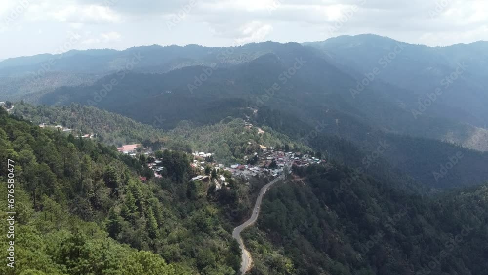 Aerial Take from over the forest trees to a town in the mountains.