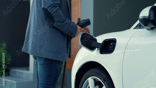 Progressive man attaches an emission-free power connector to the battery of electric vehicle at his home. Electric vehicle charging via cable from charging station to EV car battery © Summit Art Creations
