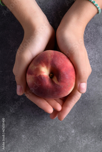 Authentic female hands holding a fresh ripe peach on a gray table background, close up. Healthy summer snack, food lifestyle