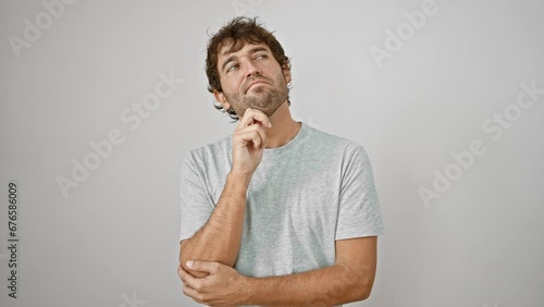 Thoughtful young man in t-shirt, hand rested on chin, sporting a pensive smile. in the sea of doubt, he's mulling over a tricky question. a casual, isolated snapshot on a crisp white background.
