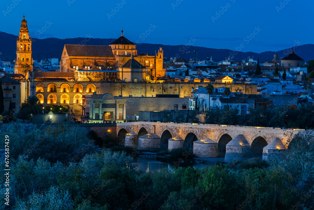 Mosque-cathedral of Cordoba and the Roman bridge illuminated in the blue hour, before dusk.
