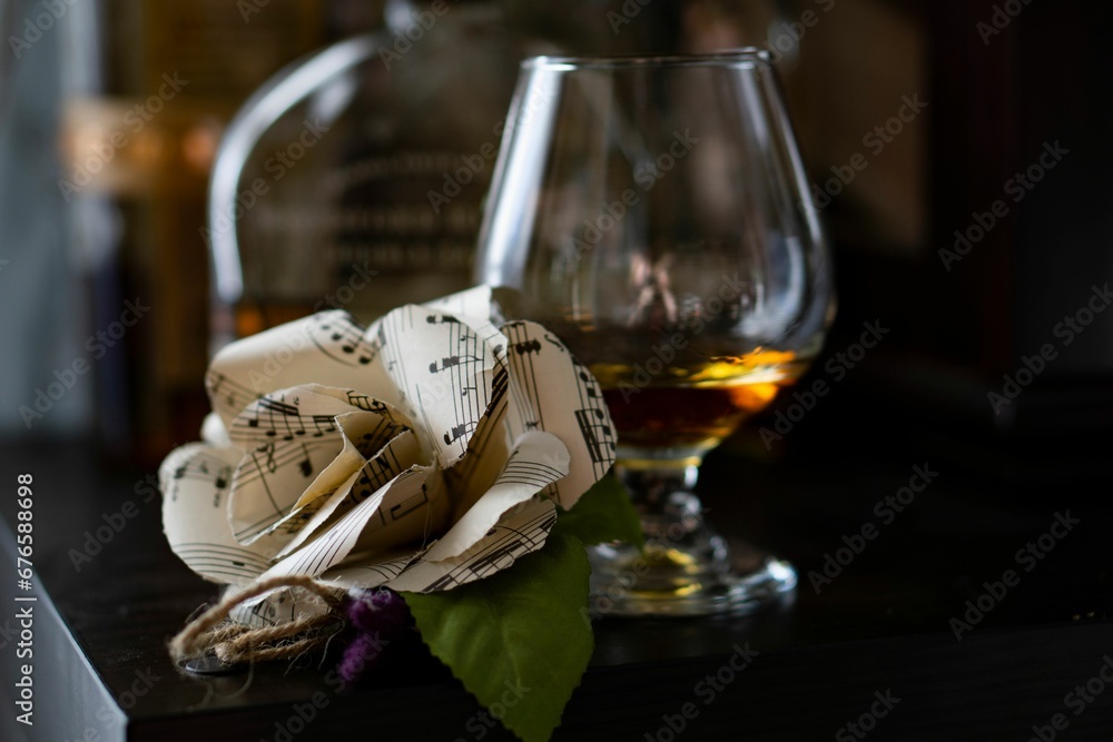 Closeup of sheet music boutonniere next to a glass of whiskey on the table - obrazy, fototapety, plakaty 