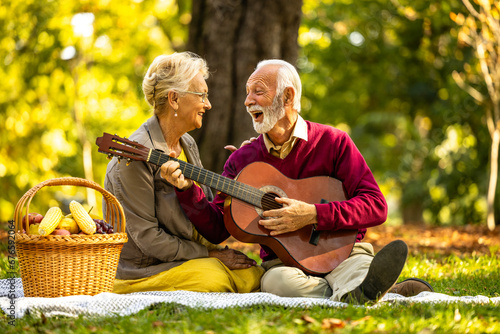 Elderly couple in love on picnic enjoying autumn and relaxing with guitar.