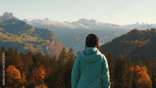 Female hiker standing on edge of hill and looking at snowy swiss Alps mountains photo