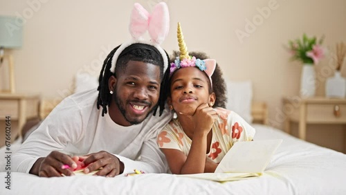 African american father and daughter wearing funny diadem lying on bed smiling at bedroom photo
