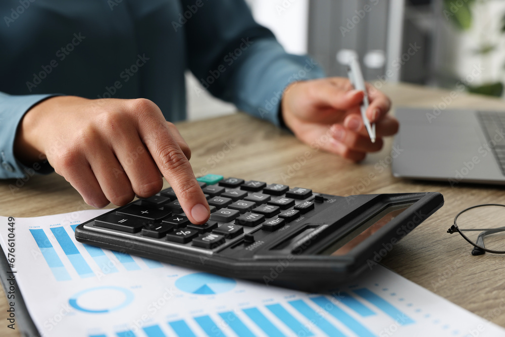 Woman using calculator at wooden table, closeup Woman using calculator at wooden table, closeup
