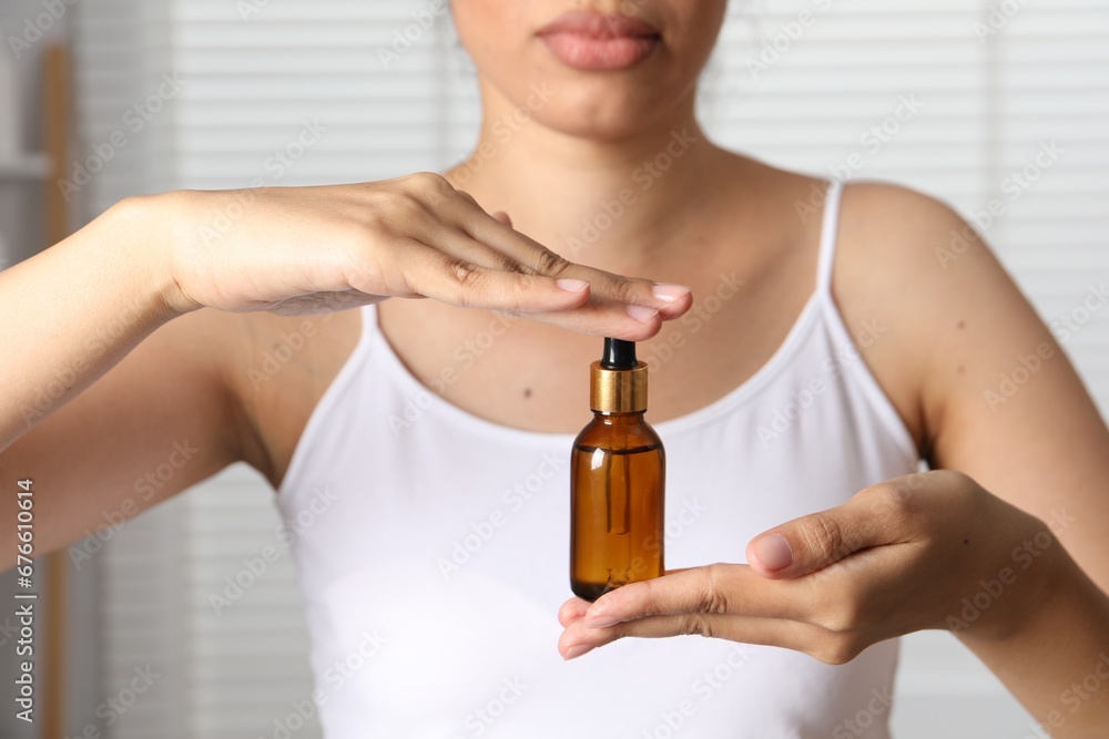 Fototapeta premium Woman with bottle of cosmetic serum on blurred background, closeup