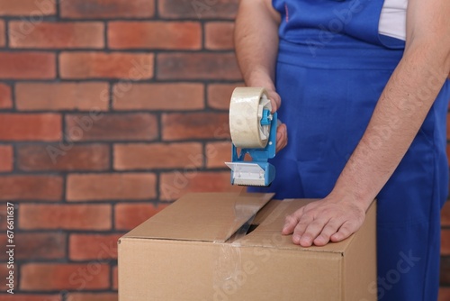 Worker taping box with adhesive tape dispenser near brick wall, closeup