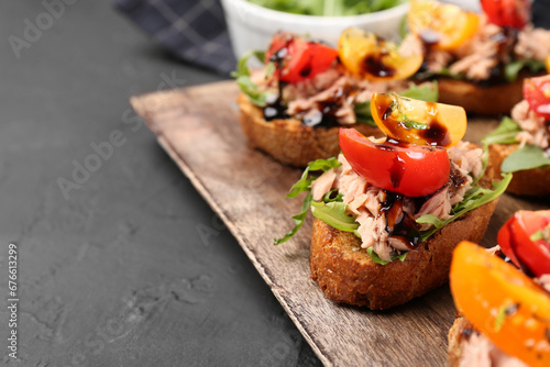 Delicious bruschettas with balsamic vinegar, tomatoes, arugula and tuna on grey textured table, closeup. Space for text