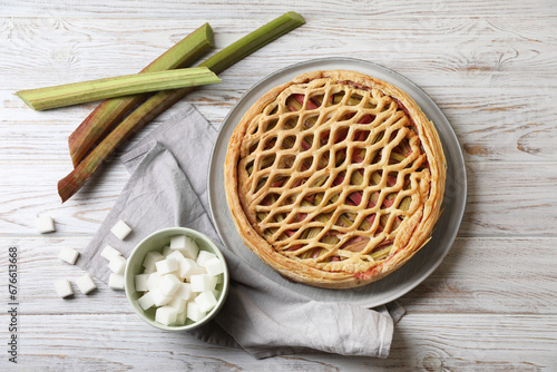 Freshly baked rhubarb pie, stalks and sugar cubes on light wooden table, flat lay