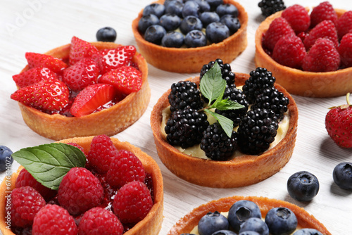 Tartlets with different fresh berries on white wooden table, closeup. Delicious dessert