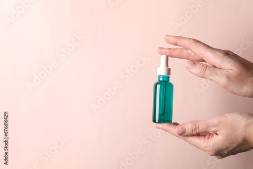 Woman with bottle of cosmetic serum on light pink background, closeup. Space for text