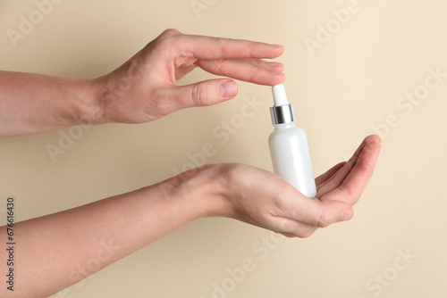 Woman with bottle of cosmetic serum on beige background  closeup