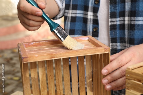 Man applying varnish onto wooden crate against blurred background, closeup