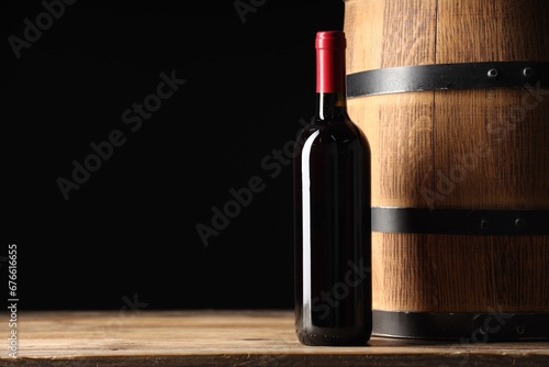 Bottle of delicious wine and wooden barrel on table against black background. Space for text © New Africa