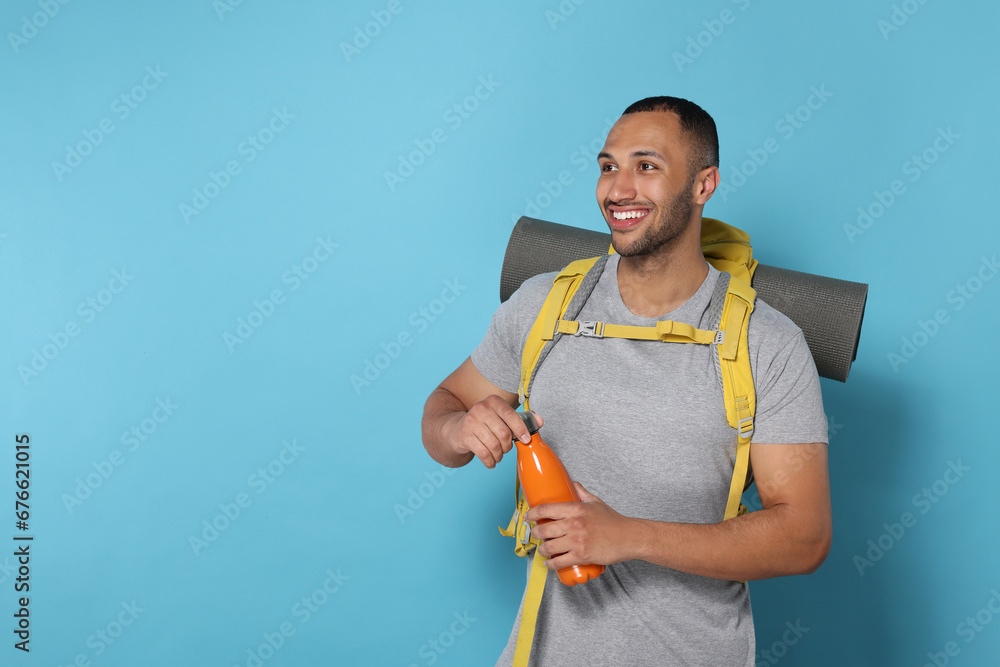 Happy tourist with backpack and thermo bottle on light blue background, space for text Happy tourist with backpack and thermo bottle on light blue background, space for text