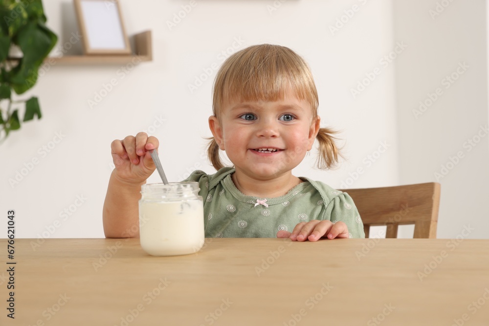 Cute little child eating tasty yogurt with spoon from jar at wooden table Cute little child eating tasty yogurt with spoon from jar at wooden table
