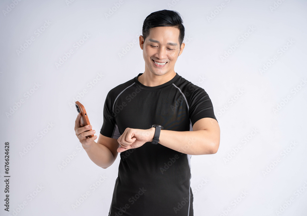 Fototapeta premium Portrait of a man wearing sports clothes, holding a phone and posing on a white background