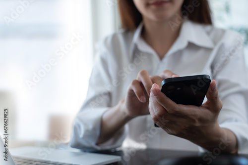 Close up of businesswoman using mobile smart phone during working on laptop computer at office. Asian business woman hand holding smartphone, connecting the internet