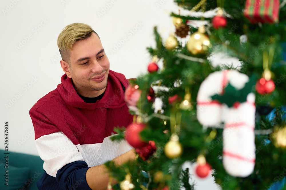 young man decorating Christmas tree at home young man decorating Christmas tree at home