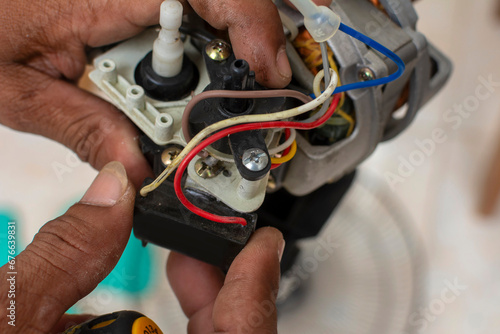 A technician checks a defective capacitor of an old oscillating electric fan. Cleaning and repairing an electric stand fan. Top view.