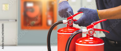 Fotografia Fire extinguisher has hand engineer checking pressure gauges with exit door to prepare fire equipment for protection in emergency case and safety or rescue and alarm system training concept