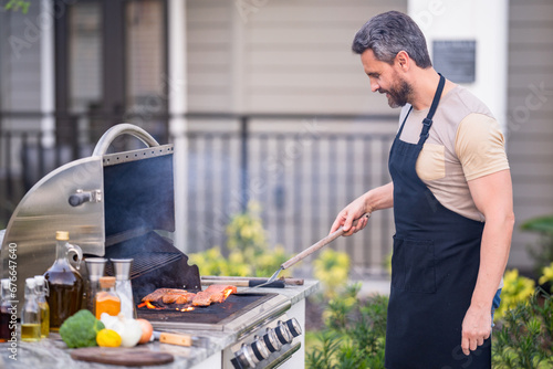 BBQ, grilling, barbecue outside. Man with barbeque roast fish outdoor. Grilling and barbecue concept. Bbq and grill. Man in barbecue preparing fish salmon. Chef cooking barbecuing seafood. photo