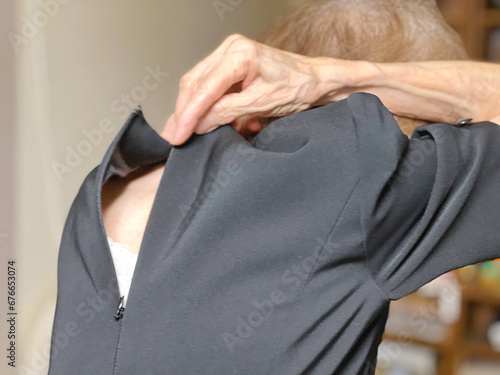 喪服の背中のファスナーを上げようとしている高齢女性の手元