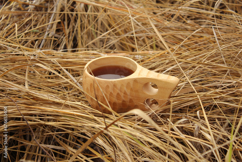Wooden Finnish mug with tea on dry grass