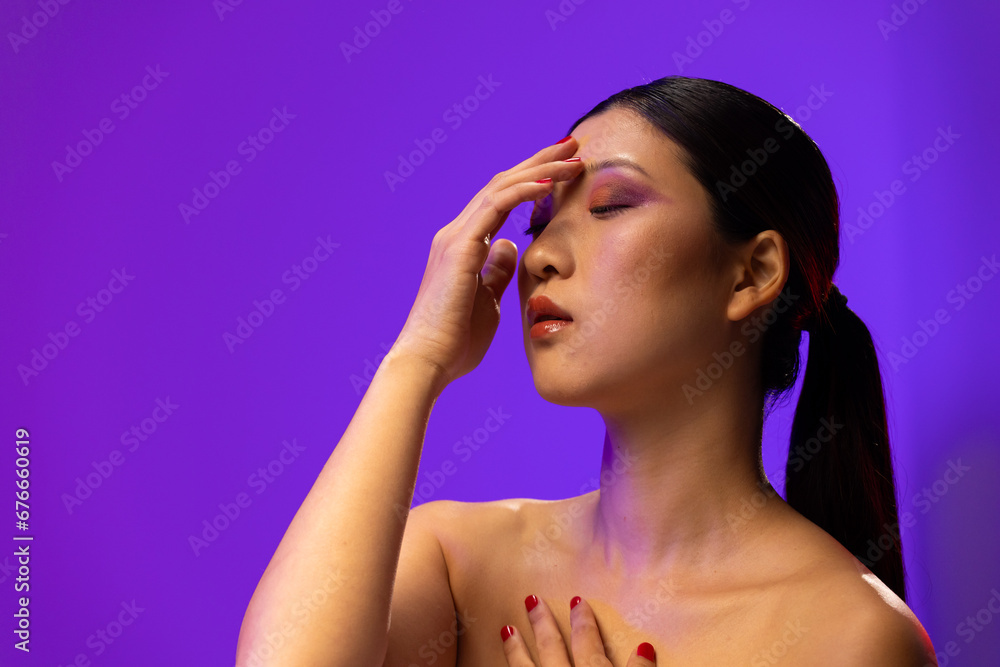 Asian woman with black hair wearing purple eye shadow and red nail polish on purple background